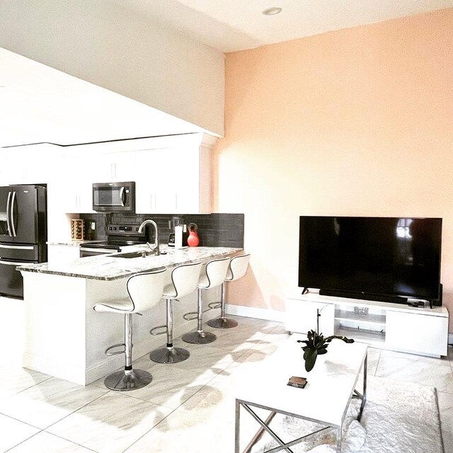 kitchen with black appliances, a breakfast bar, kitchen peninsula, white cabinetry, and light stone counters