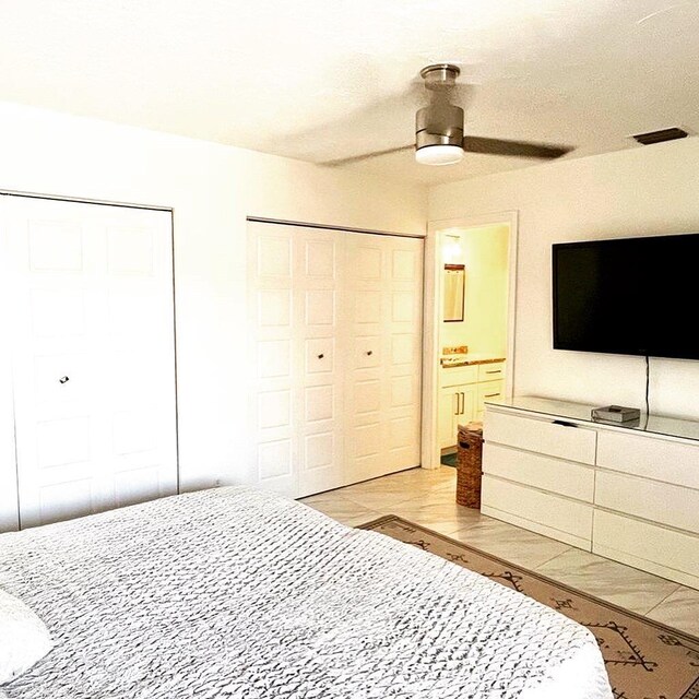 bedroom with two closets, ceiling fan, ensuite bathroom, and light hardwood / wood-style floors