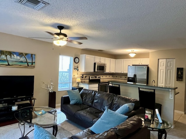 living area featuring baseboards, visible vents, ceiling fan, and a textured ceiling