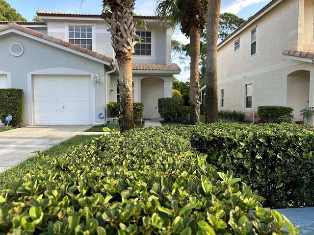 mediterranean / spanish house with driveway, a tiled roof, stucco siding, and an attached garage