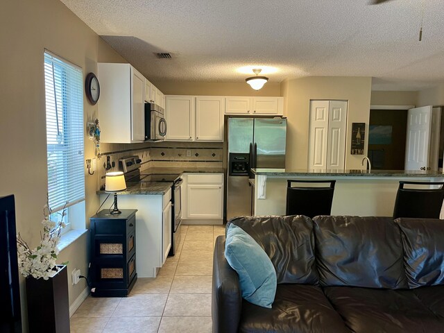 kitchen featuring white cabinetry, a kitchen breakfast bar, stainless steel refrigerator with ice dispenser, a textured ceiling, and light tile patterned flooring