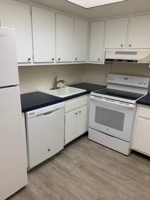 kitchen with white cabinets, white appliances, light hardwood / wood-style floors, and sink