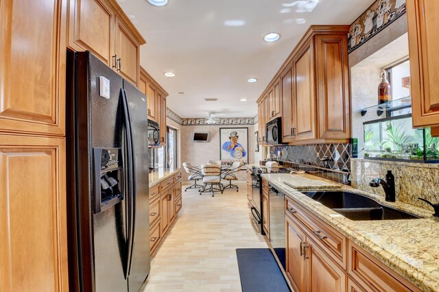 kitchen featuring light stone countertops, black appliances, light hardwood / wood-style flooring, backsplash, and sink