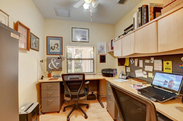 office area with a textured ceiling, built in desk, ceiling fan, and light hardwood / wood-style floors