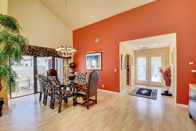 dining area featuring light wood-type flooring, high vaulted ceiling, a notable chandelier, a textured ceiling, and french doors