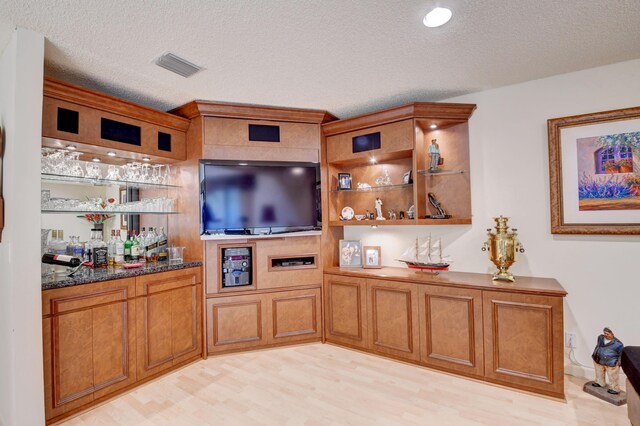 bar featuring dark stone counters, a textured ceiling, and light hardwood / wood-style flooring