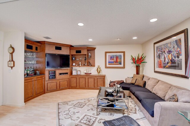 living room featuring a textured ceiling, bar, and light wood-type flooring