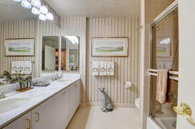 full bathroom with tile patterned floors, toilet, vanity, bath / shower combo with glass door, and a textured ceiling