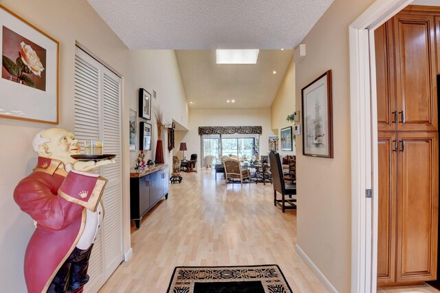 hallway featuring light wood-type flooring, a textured ceiling, and lofted ceiling with skylight