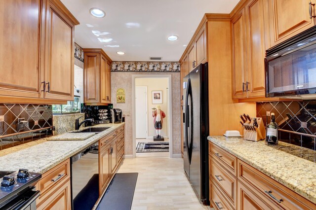 kitchen with black appliances, backsplash, sink, and light stone countertops