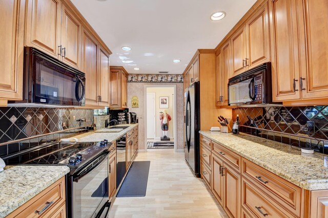 kitchen featuring light stone countertops, black appliances, tasteful backsplash, sink, and light wood-type flooring