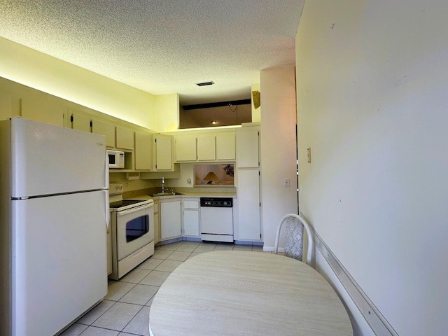 kitchen featuring light tile patterned floors, a sink, a textured ceiling, white appliances, and light countertops