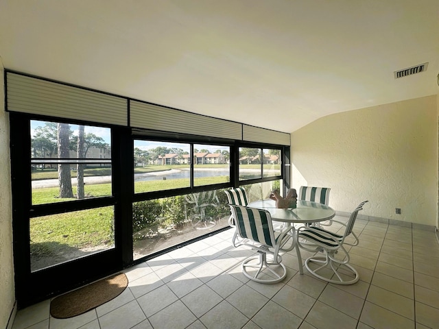 unfurnished sunroom featuring lofted ceiling, a textured wall, plenty of natural light, and visible vents