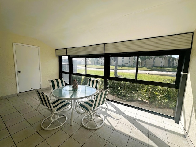 tiled dining room featuring vaulted ceiling and a textured wall