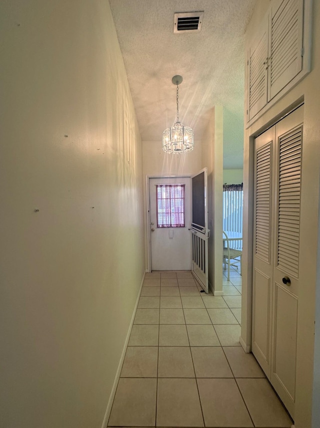 doorway with light tile patterned floors, a textured ceiling, visible vents, baseboards, and a chandelier