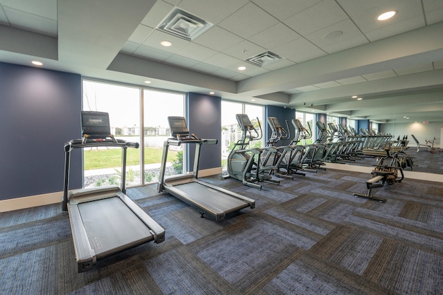 gym featuring a raised ceiling, a paneled ceiling, and dark colored carpet