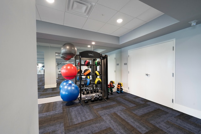 exercise room featuring a paneled ceiling and dark carpet