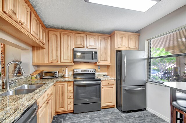 kitchen featuring light brown cabinets, sink, light stone countertops, a textured ceiling, and appliances with stainless steel finishes