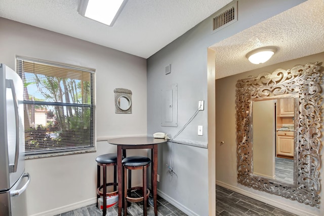 interior space featuring stainless steel fridge, electric panel, a textured ceiling, light brown cabinets, and dark hardwood / wood-style floors