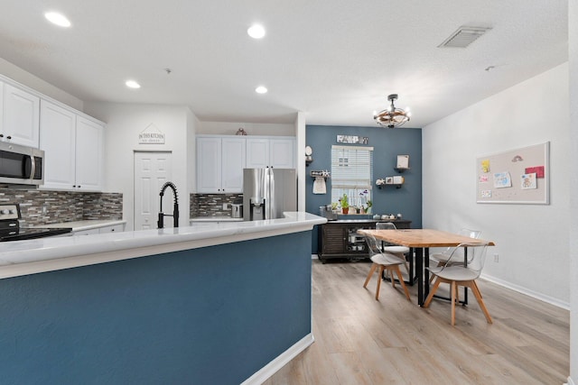 kitchen with white cabinets, backsplash, stainless steel appliances, and a notable chandelier