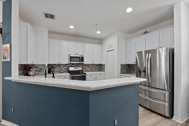 kitchen featuring kitchen peninsula, white cabinetry, stainless steel appliances, and light wood-type flooring