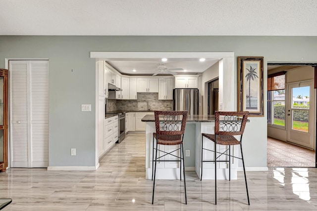 kitchen with a breakfast bar area, white cabinetry, backsplash, stainless steel appliances, and a textured ceiling