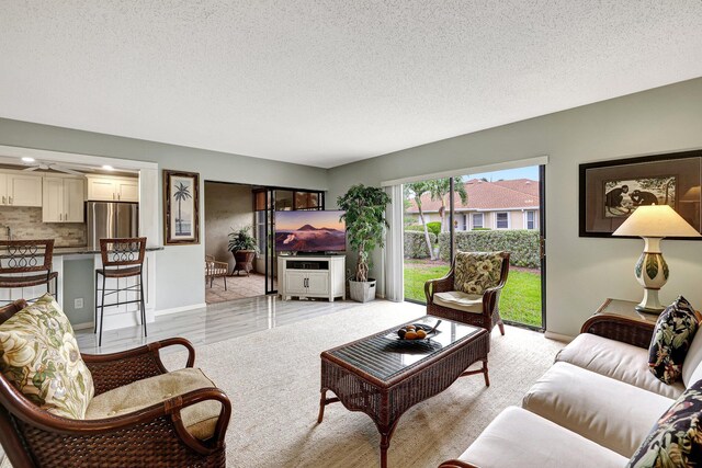 living room with ceiling fan, a textured ceiling, and light hardwood / wood-style flooring