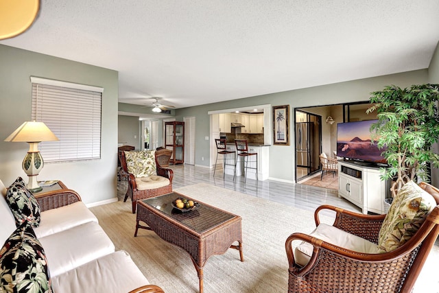 living room featuring ceiling fan, a textured ceiling, and light hardwood / wood-style flooring