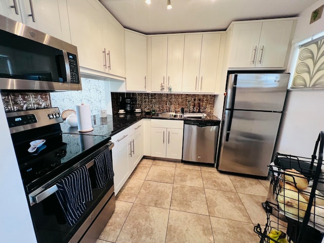 kitchen featuring appliances with stainless steel finishes, backsplash, light tile patterned floors, dark stone countertops, and white cabinets