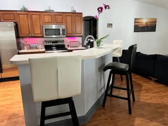 kitchen with wood-type flooring, stainless steel appliances, a kitchen bar, and kitchen peninsula