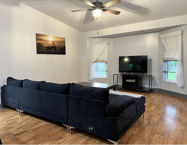 living room with wood-type flooring, vaulted ceiling, ceiling fan, and a textured ceiling