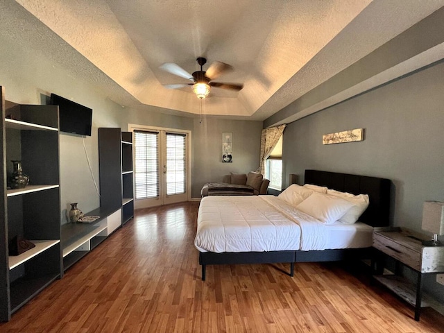 bedroom with a textured ceiling, a raised ceiling, hardwood / wood-style floors, ceiling fan, and french doors