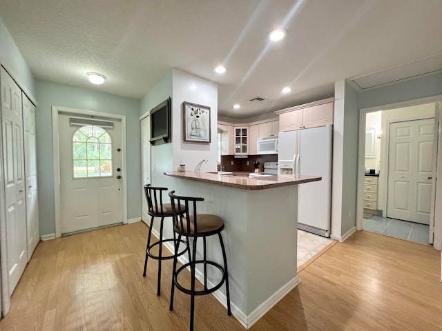 kitchen with light hardwood / wood-style flooring, white appliances, kitchen peninsula, and white cabinetry