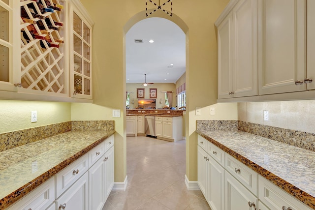 kitchen featuring dishwasher, light stone counters, white cabinets, hanging light fixtures, and light tile patterned floors