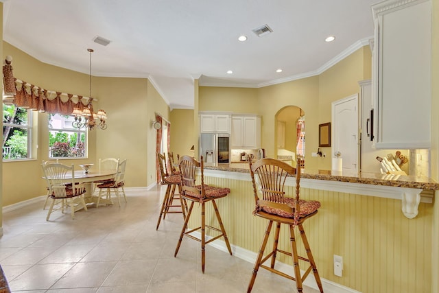 kitchen with stainless steel fridge, white cabinetry, light stone counters, a kitchen bar, and decorative light fixtures