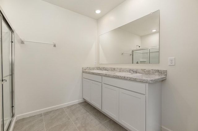 full bathroom featuring a stall shower, tile patterned floors, a sink, baseboards, and double vanity