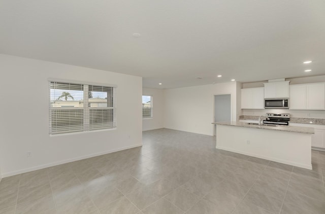 kitchen featuring light stone countertops, stainless steel appliances, recessed lighting, white cabinetry, and open floor plan