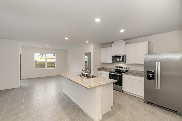 kitchen with appliances with stainless steel finishes, white cabinetry, an island with sink, a sink, and light tile patterned floors