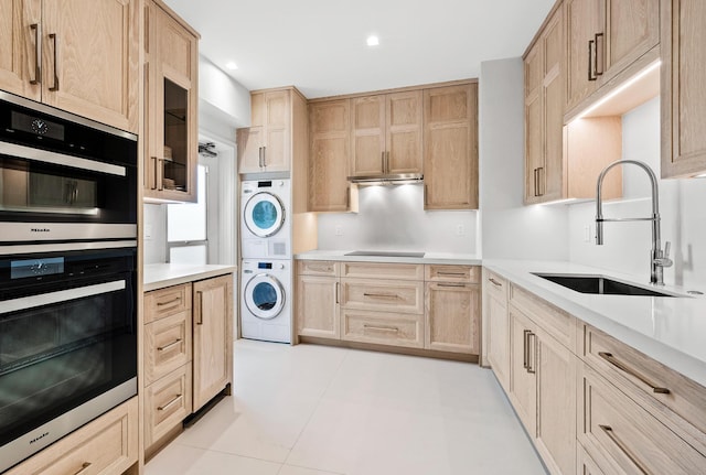 kitchen with sink, light brown cabinetry, light tile patterned floors, double oven, and stacked washer and clothes dryer