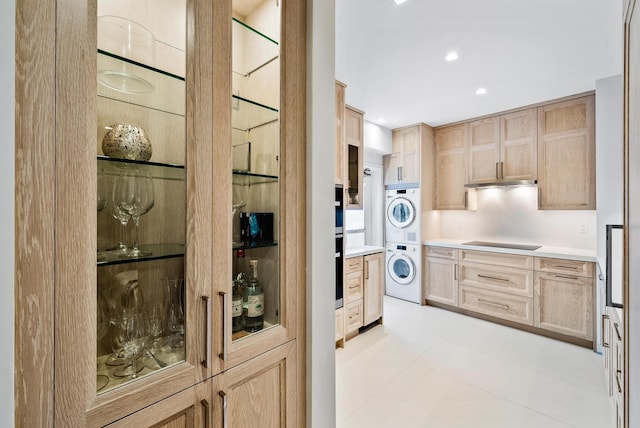 kitchen with black electric stovetop, light tile patterned flooring, stacked washer and dryer, and light brown cabinets