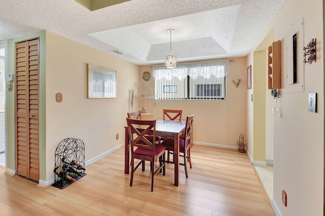 dining space with baseboards, visible vents, a textured ceiling, a raised ceiling, and light wood-type flooring