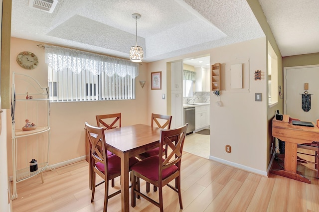 dining room with a tray ceiling, visible vents, light wood finished floors, and a textured ceiling