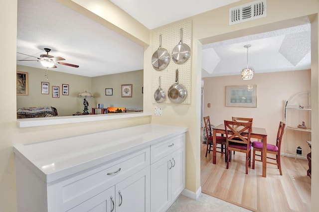 kitchen featuring visible vents, light countertops, white cabinets, light wood-style floors, and decorative light fixtures