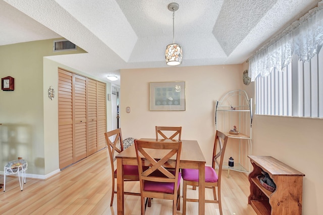 dining area featuring a tray ceiling, light wood-type flooring, and a textured ceiling