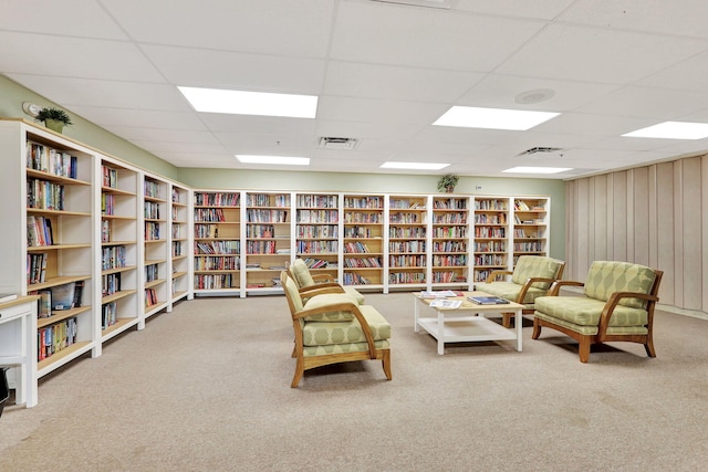 sitting room featuring visible vents, carpet flooring, wooden walls, and wall of books