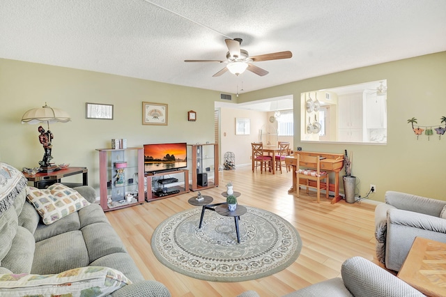 living room featuring ceiling fan, visible vents, a textured ceiling, and wood finished floors