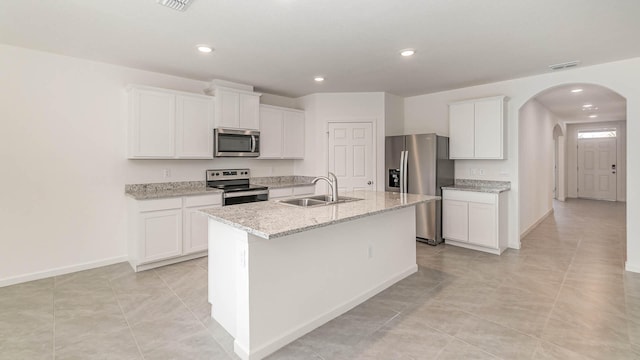 kitchen with appliances with stainless steel finishes, an island with sink, white cabinets, light stone countertops, and sink