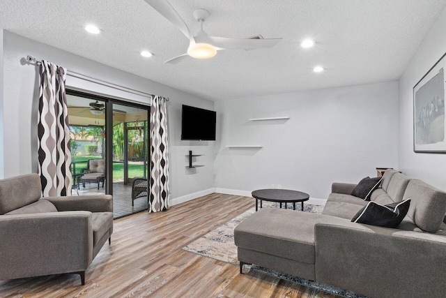 living room with a textured ceiling, ceiling fan, and light hardwood / wood-style flooring