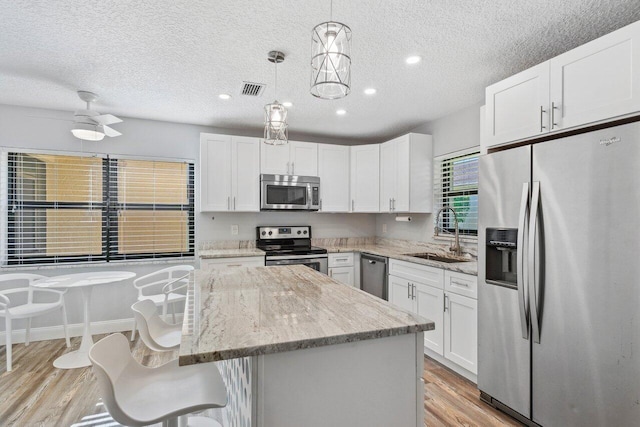 kitchen featuring pendant lighting, stainless steel appliances, white cabinetry, and a textured ceiling