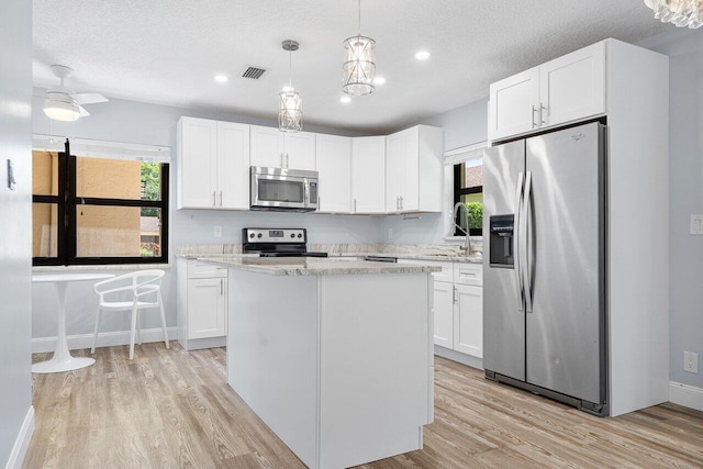 kitchen featuring pendant lighting, light wood-type flooring, white cabinets, appliances with stainless steel finishes, and light stone countertops